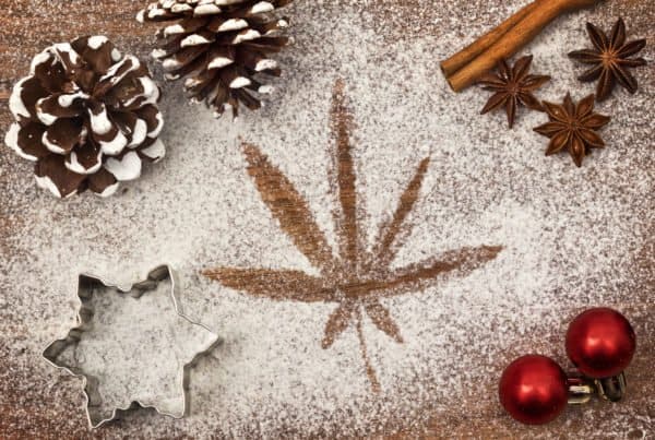 Cannabis leaf on a snowy background with pine cones and ornaments, perfect for Christmas enthusiasts.
