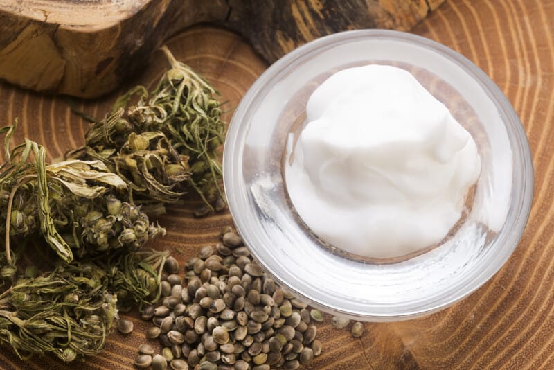 cbd cream in a glass jar with cannabis buds and seeds