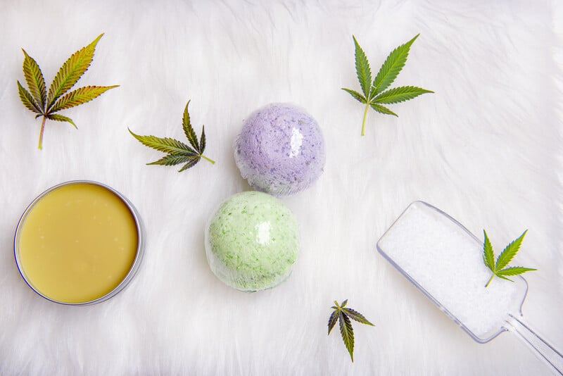 cannabis leaves, bath bombs, salt and topicals on white table