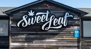 Wood paneling store front with Sweet Leaf marijuana dispensary logo in white.