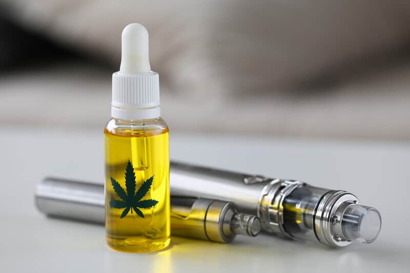 Vape Pens on grey table with a marijuana tincture bottle.