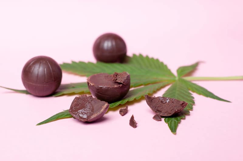 chocolate balls and cannabis leaf on purple background, marijuana chocolate bars