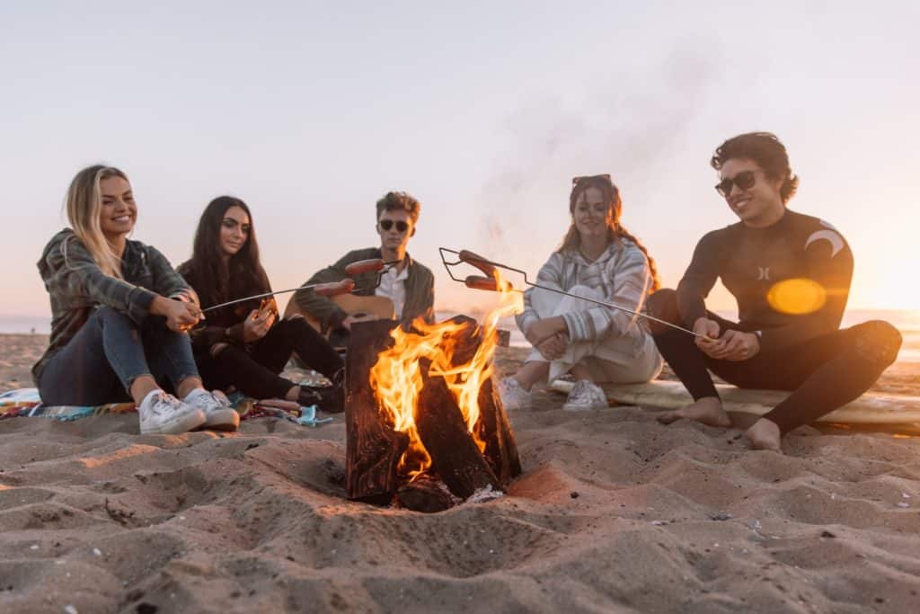 people sitting around a bonfire on the beach, new cannabis strains for summer