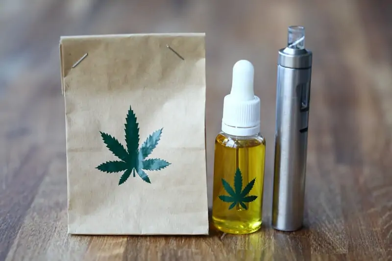 bag with weed leaf on it, cannabis tincture, and vape pen on wood table, Marijuana Edibles vs Cannabis Tincture vs Vape