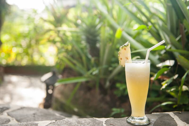 tropical drink with pineapple in it against shrubs, cannabis quencher