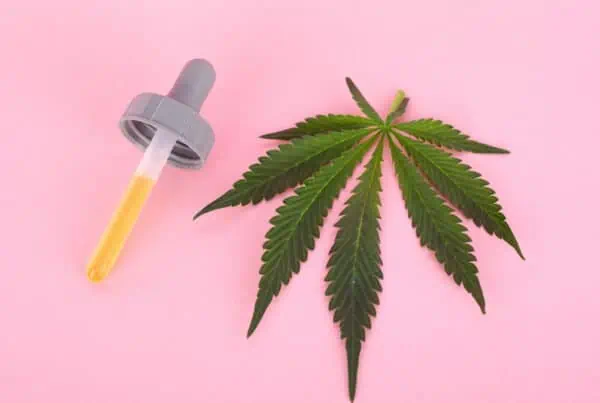 cannabis leave next to a dropper on pink, how to make a marijuana tincture