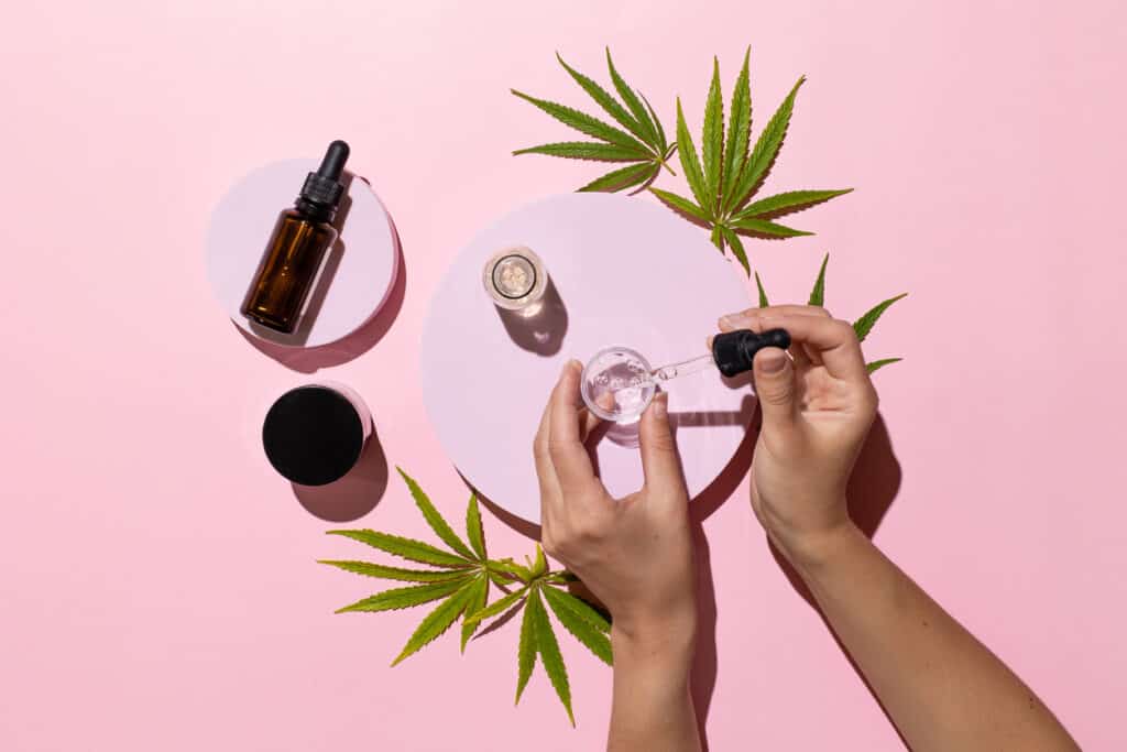 cannabis tincture recipes. Bottles with CBD oil, THC tincture and cannabis leaves on pink background. Alternative cosmetics medical concept